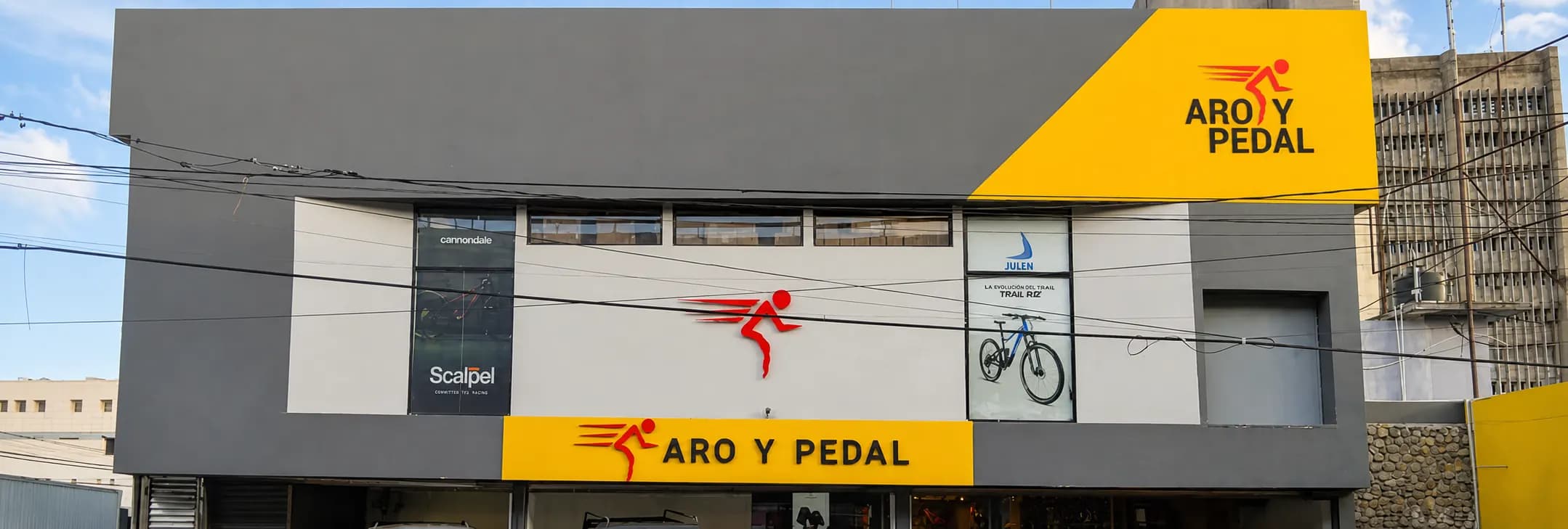 Storefront of the Aro y Pedal shop on 27 de Febrero avenue, Santo Domingo: yellow sign with the logo on the corner and the yellow Aro y Pedal band over the entrance